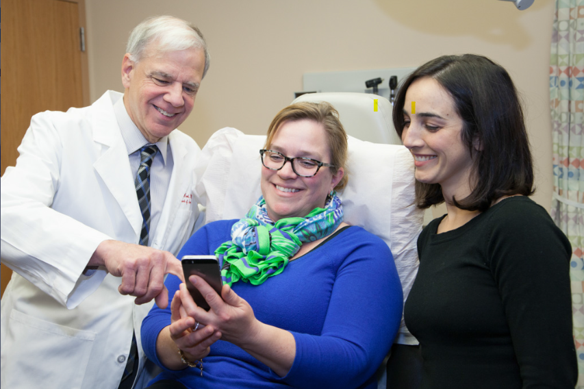 doctor and patient interfacing with mobile app as researcher look on